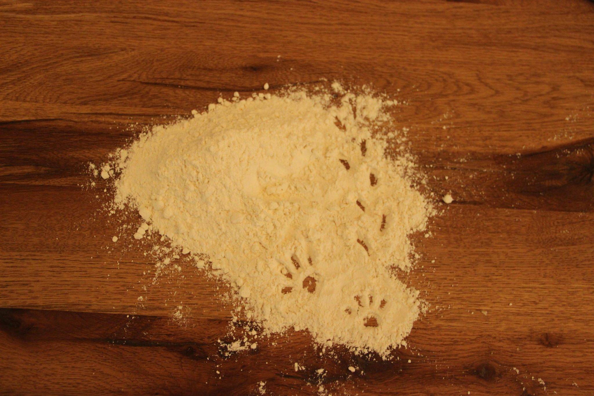 Un montón de harina en una mesa de madera con huellas de gato y ratón