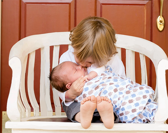 Sibling kissing newborn baby