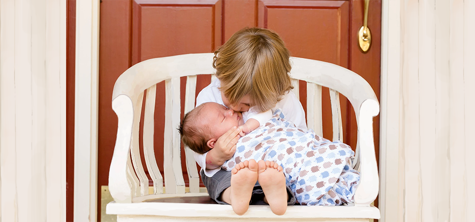 Sibling kissing newborn baby