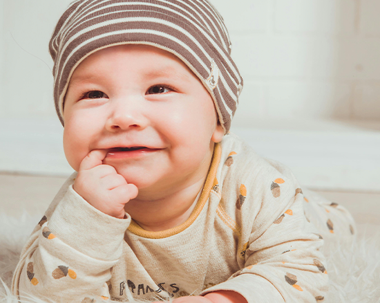 A little baby boy with his finger in his mouth, smiling