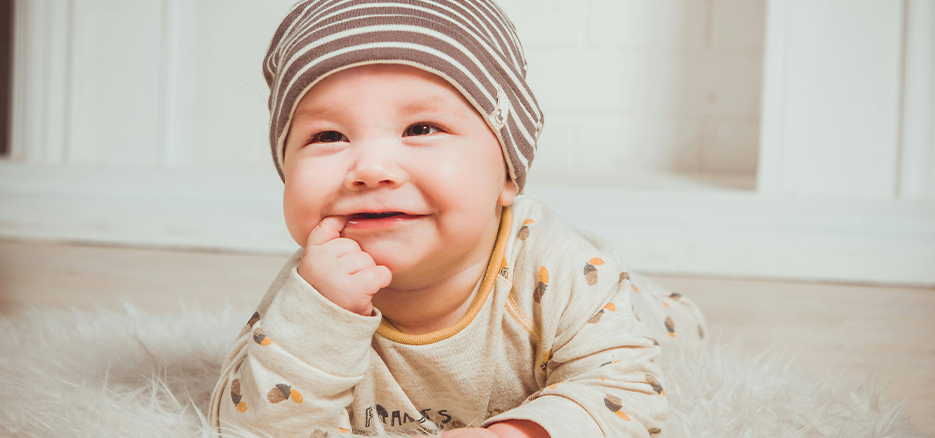 A little baby boy with his finger in his mouth, smiling
