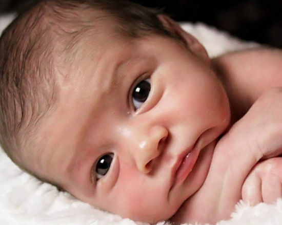 Newborn baby lying on a soft white blanket, looking attentively at the camera