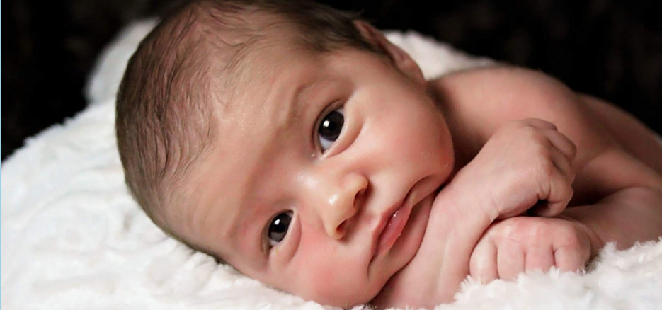 Newborn baby lying on a soft white blanket, looking attentively at the camera